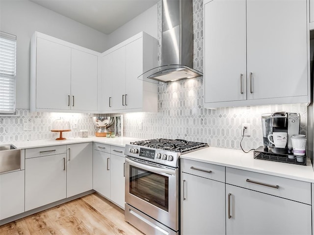 kitchen featuring wall chimney exhaust hood, white cabinetry, tasteful backsplash, stainless steel gas stove, and light wood-type flooring