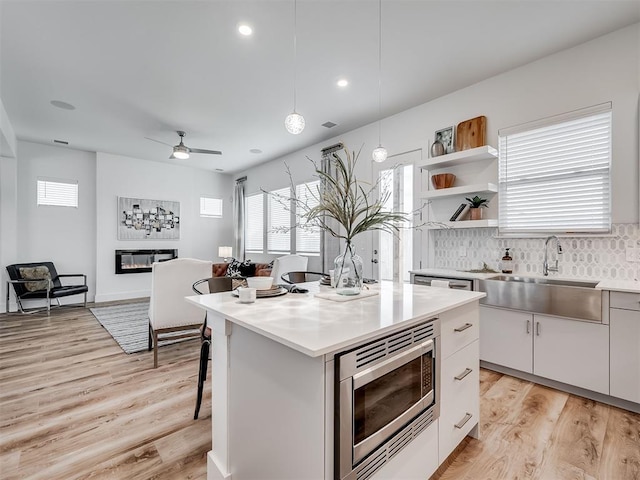 kitchen with white cabinetry, stainless steel microwave, decorative light fixtures, a kitchen island, and sink