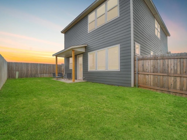 back house at dusk with a patio area and a yard