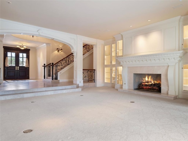 unfurnished living room with a premium fireplace, french doors, carpet floors, and ornamental molding