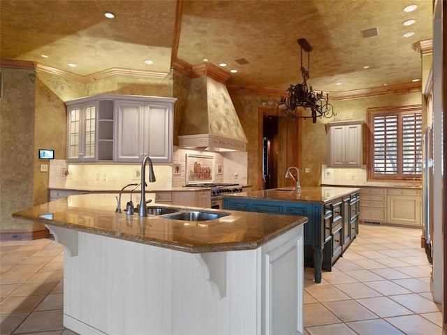 kitchen with premium range hood, a breakfast bar, a center island with sink, and a notable chandelier