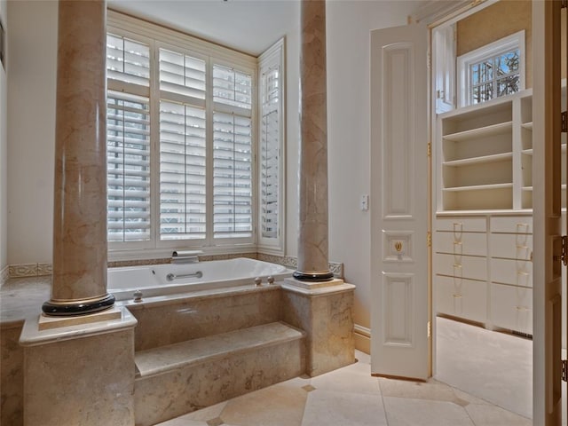 bathroom with decorative columns, tiled tub, and tile patterned flooring