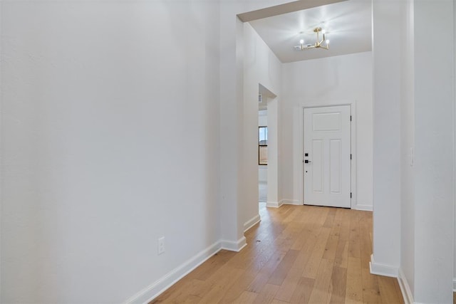 corridor with an inviting chandelier and light hardwood / wood-style flooring