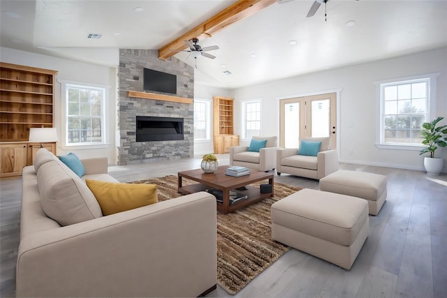 living room with vaulted ceiling with beams, hardwood / wood-style flooring, a stone fireplace, and ceiling fan