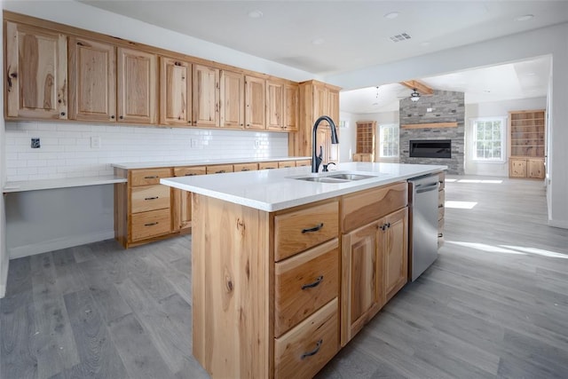 kitchen featuring sink, a kitchen island with sink, stainless steel dishwasher, decorative backsplash, and light wood-type flooring