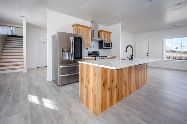 kitchen with a kitchen island with sink, wall chimney range hood, sink, light wood-type flooring, and stainless steel appliances