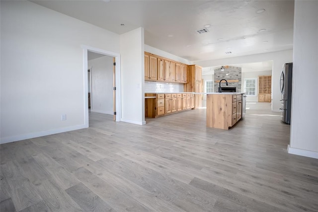 kitchen featuring decorative backsplash, stainless steel fridge, light brown cabinets, and light hardwood / wood-style flooring