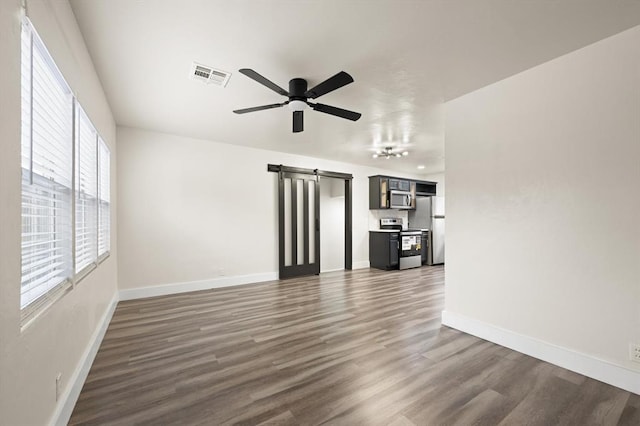 unfurnished living room featuring a barn door, ceiling fan, and dark wood-type flooring