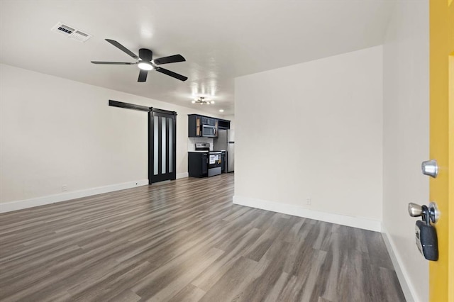 unfurnished living room with ceiling fan, a barn door, and dark wood-type flooring