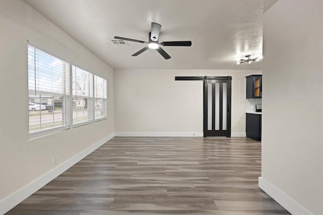 empty room featuring a barn door, ceiling fan, and dark wood-type flooring