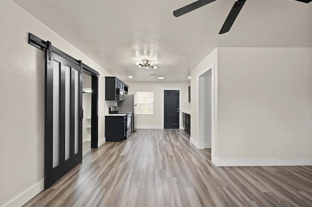 unfurnished living room with a barn door, light hardwood / wood-style floors, and ceiling fan