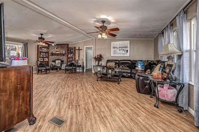 living room with a fireplace, a textured ceiling, light hardwood / wood-style floors, and ceiling fan