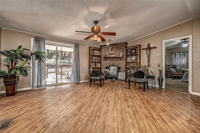 unfurnished room with crown molding, ceiling fan, a fireplace, a textured ceiling, and light hardwood / wood-style floors