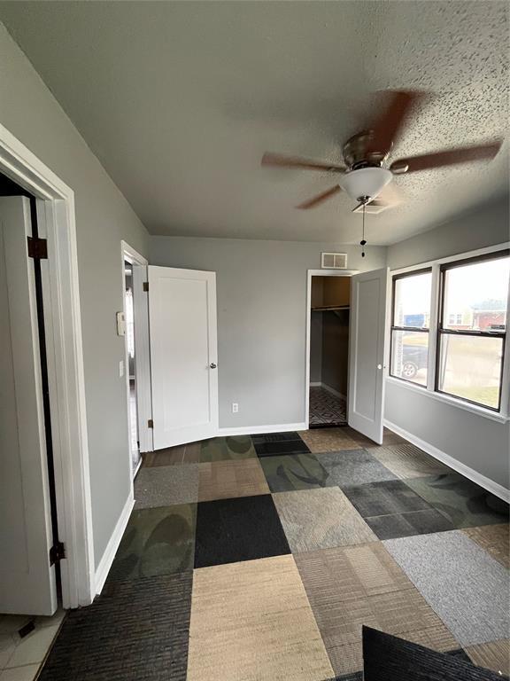 unfurnished bedroom featuring ceiling fan, a textured ceiling, and dark colored carpet