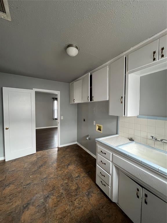 kitchen featuring white cabinetry, sink, tile countertops, a textured ceiling, and decorative backsplash