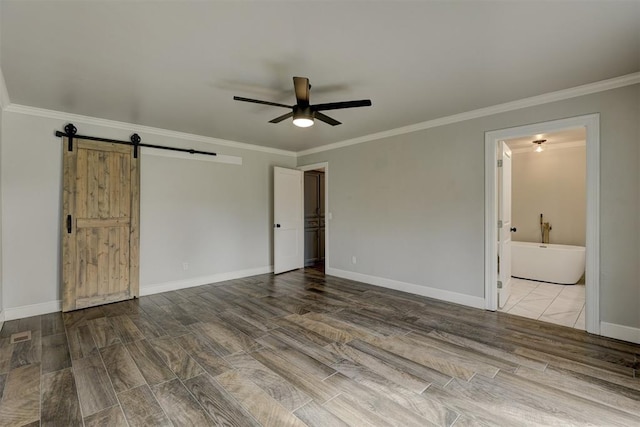 unfurnished bedroom with light wood-type flooring, ensuite bath, ornamental molding, ceiling fan, and a barn door