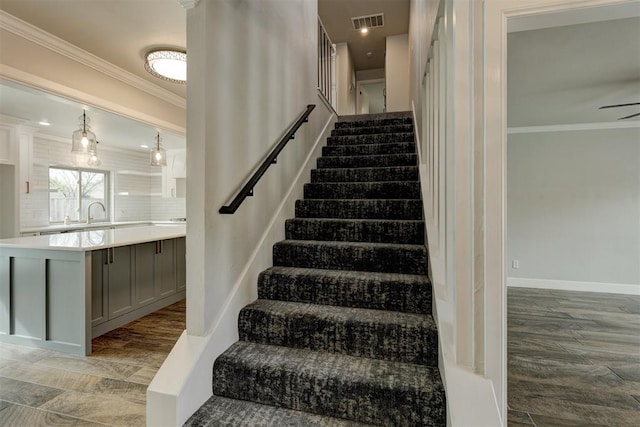 stairs featuring hardwood / wood-style flooring, ceiling fan, crown molding, and sink