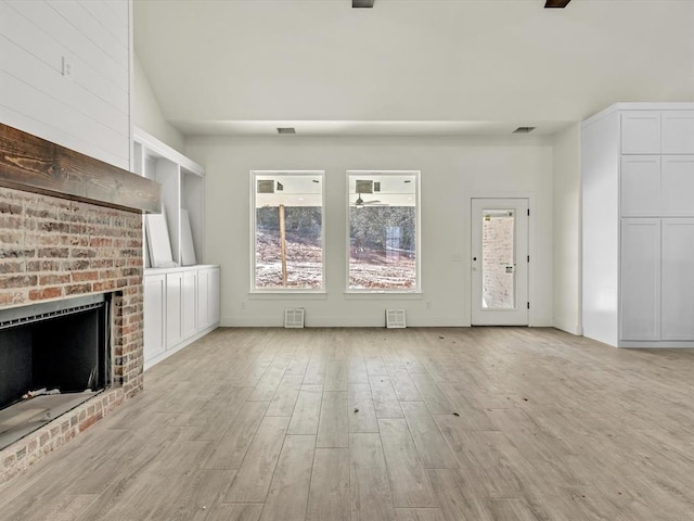 unfurnished living room with light wood-type flooring, a brick fireplace, and visible vents