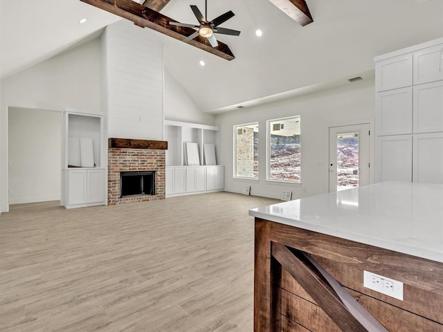 living area featuring beam ceiling, a brick fireplace, light wood-style flooring, and a ceiling fan