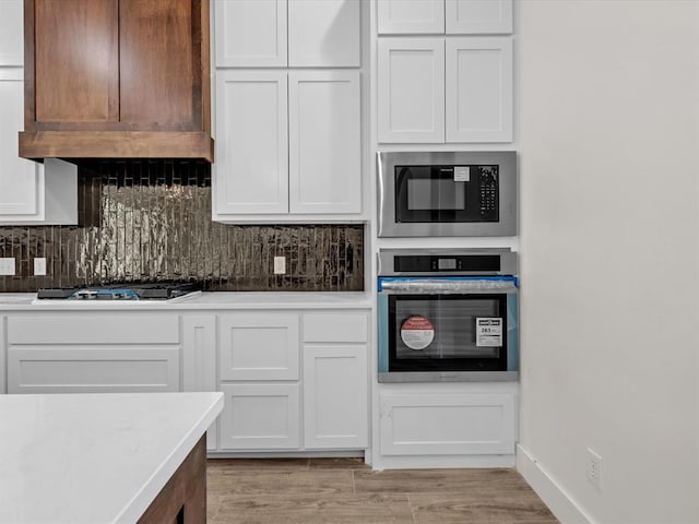 kitchen featuring tasteful backsplash, oven, built in microwave, gas stovetop, and white cabinetry