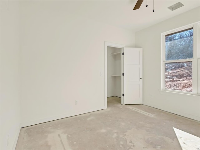 unfurnished bedroom featuring a spacious closet, unfinished concrete flooring, and a ceiling fan