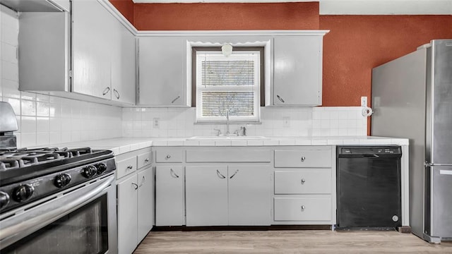 kitchen with dishwasher, tile counters, sink, gas range oven, and stainless steel fridge