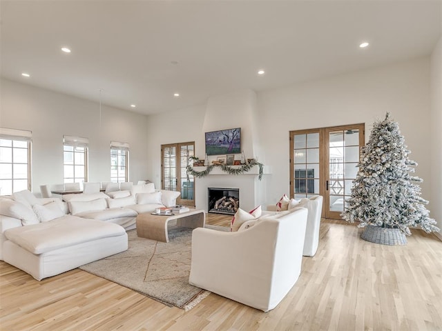 living room with a large fireplace, light hardwood / wood-style floors, and french doors