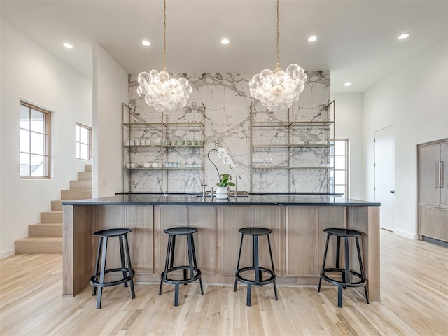 kitchen with a kitchen breakfast bar, a towering ceiling, light wood-type flooring, pendant lighting, and a notable chandelier