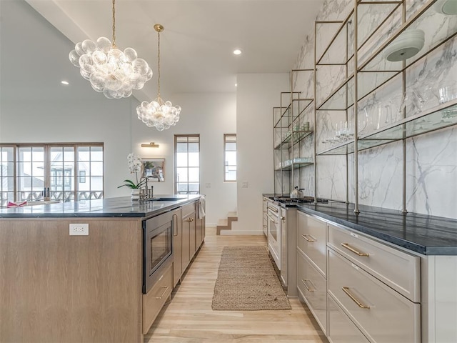 kitchen with a kitchen island with sink, sink, light hardwood / wood-style flooring, appliances with stainless steel finishes, and a chandelier