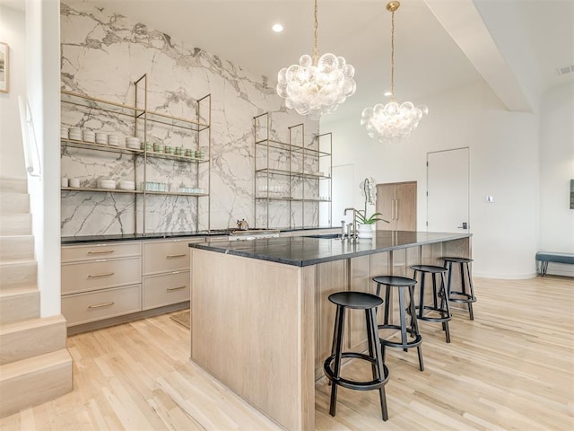 kitchen featuring an island with sink, a chandelier, pendant lighting, light hardwood / wood-style floors, and light brown cabinetry