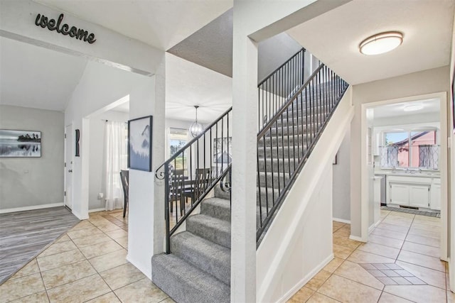 stairway featuring tile patterned flooring, a notable chandelier, and vaulted ceiling