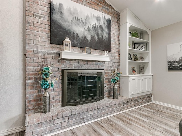 unfurnished living room featuring built in shelves, light wood-type flooring, lofted ceiling, and a brick fireplace