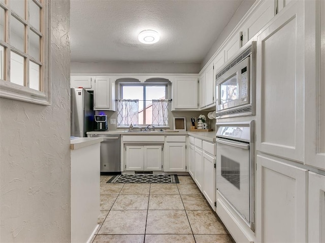 kitchen with a textured ceiling, stainless steel appliances, and white cabinetry