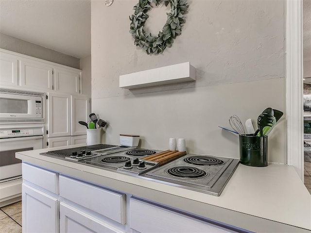 kitchen with white cabinetry, light tile patterned flooring, and white appliances