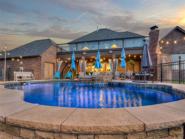 pool at dusk featuring an in ground hot tub, a patio, and pool water feature