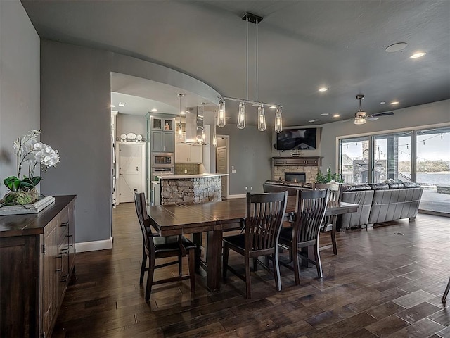 dining room with a stone fireplace, ceiling fan, and dark hardwood / wood-style flooring