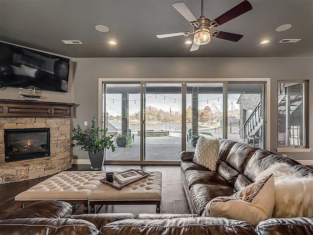 living room with hardwood / wood-style flooring, a stone fireplace, and ceiling fan