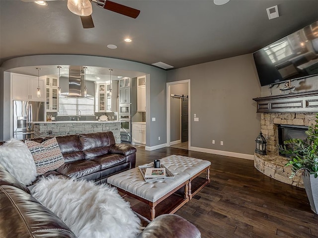 living room with sink, dark hardwood / wood-style floors, ceiling fan, a barn door, and a fireplace