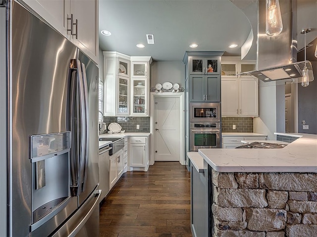 kitchen featuring island range hood, light stone counters, white cabinetry, and appliances with stainless steel finishes