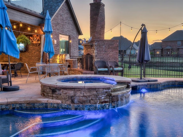 pool at dusk with a patio area, an in ground hot tub, pool water feature, and exterior kitchen