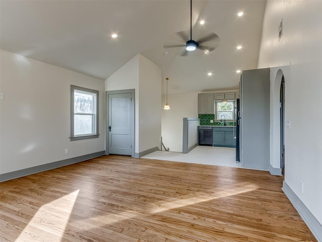 unfurnished living room with light hardwood / wood-style floors, high vaulted ceiling, ceiling fan, and sink