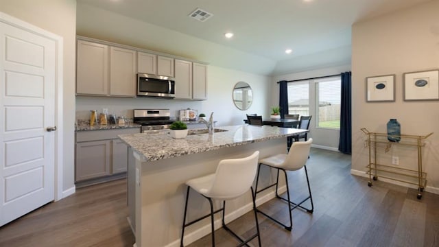 kitchen featuring stainless steel appliances, visible vents, an island with sink, light stone countertops, and a kitchen breakfast bar