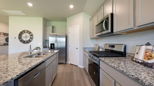 kitchen featuring light stone countertops, gray cabinets, stainless steel appliances, and a sink