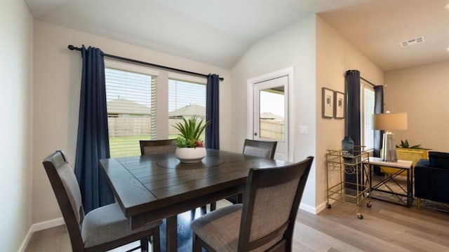 dining area with light wood finished floors, baseboards, visible vents, and vaulted ceiling