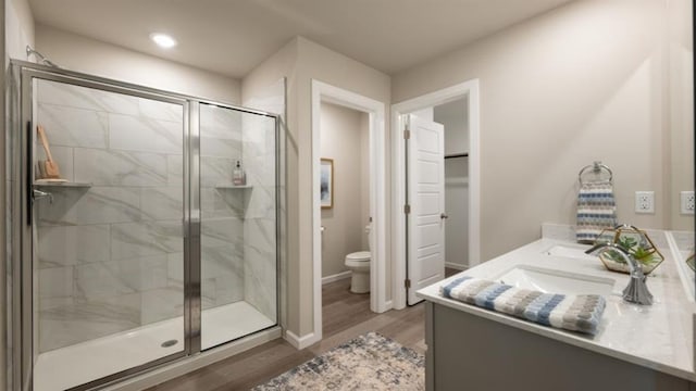 bathroom featuring toilet, wood finished floors, baseboards, double vanity, and a stall shower