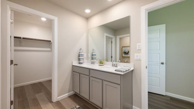 full bath featuring a walk in closet, double vanity, a sink, wood finished floors, and baseboards