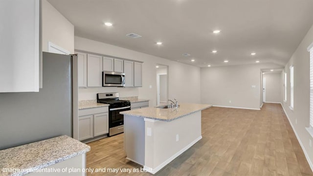 kitchen with a kitchen island with sink, stainless steel appliances, a sink, visible vents, and light stone countertops