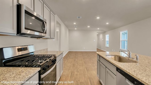 kitchen featuring light stone counters, recessed lighting, appliances with stainless steel finishes, light wood-style floors, and a sink