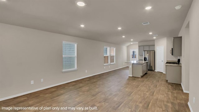 kitchen featuring a kitchen island with sink, gray cabinetry, open floor plan, light wood-type flooring, and stainless steel fridge