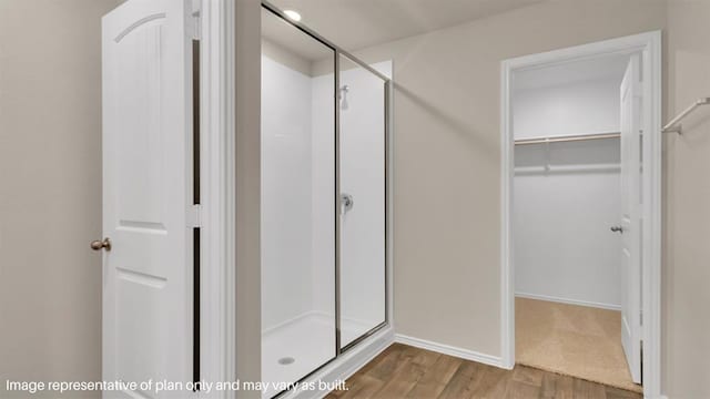 full bath featuring a shower stall, a spacious closet, baseboards, and wood finished floors